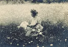 Woman with wreath of leaves in her hair sitting in a field of daisies, c1900. Creator: Unknown