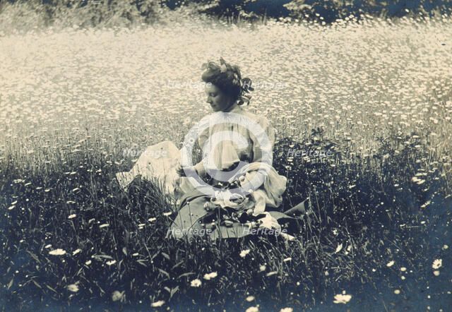 Woman with wreath of leaves in her hair sitting in a field of daisies, c1900. Creator: Unknown.
