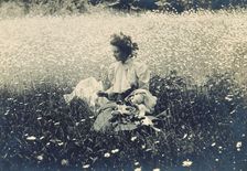Woman with wreath of leaves in her hair sitting in a field of daisies, c1900. Creator: Unknown