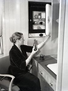 Woman using a compact fridge, possibly on board a ship, c1955. Creator: Arthur Charles Kirby Ware