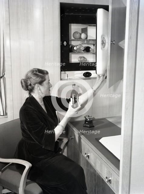 Woman using a compact fridge, possibly on board a ship, c1955.  Creator: Arthur Charles Kirby Ware.