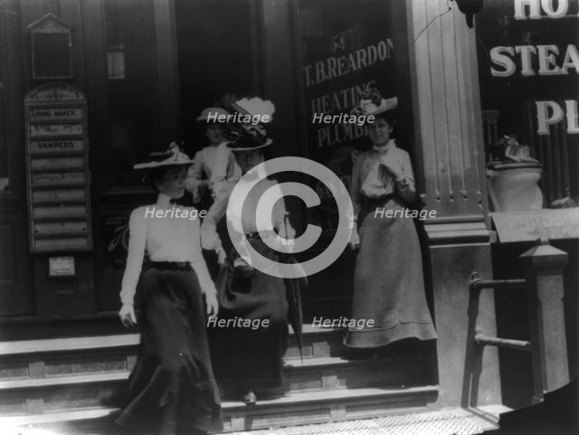 Women coming from work, Cal.?. Store window reads T.B. Reardon, heating and plumbing, 1903. Creator: Frances Benjamin Johnston.