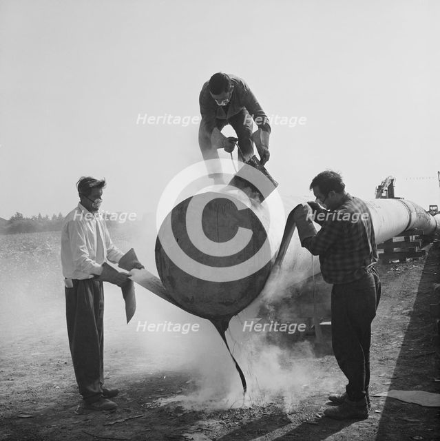 Workers wrapping and sealing the end of a steel pipe on the Fens gas pipeline, Norfolk, 24/07/1967. Creator: John Laing plc.