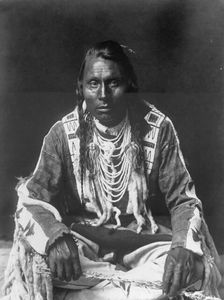 Wades in Water, Piegan Indian, full-length portrait, seated on floor, facing front..., c1910. Creator: Edward Sheriff Curtis