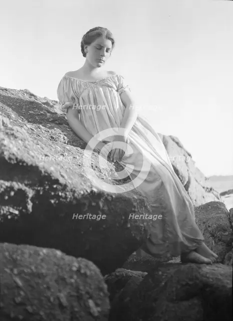 Wilson, Helen, Mrs., seated on rocks at the beach, between 1906 and 1928. Creator: Arnold Genthe.