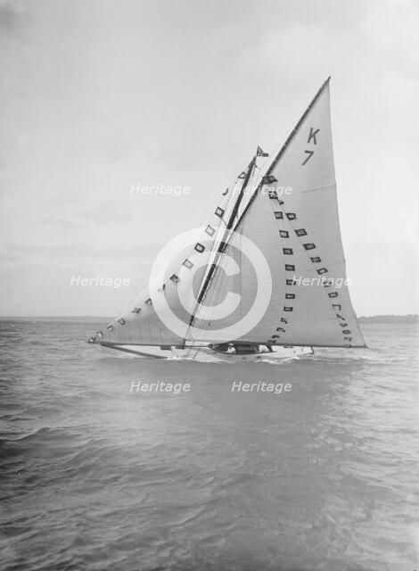 The 7 Metre 'Ginerva' (K7) under sail with prize flags, 1912. Creator: Kirk & Sons of Cowes.