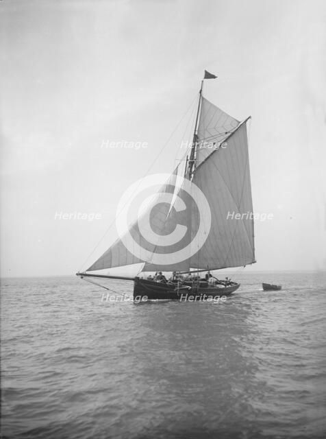 The cutter 'Citara' under sail and towing tender, 1911. Creator: Kirk & Sons of Cowes.