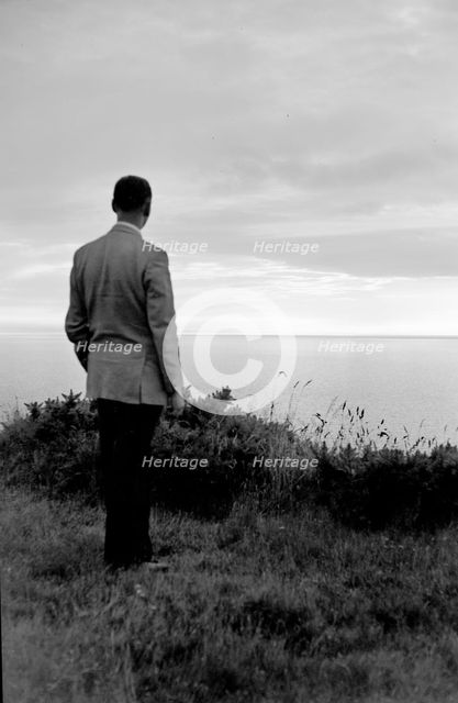 The silhouette of a man standing on a cliff top watching the sunset over the sea, c1945-c1965. Artist: SW Rawlings