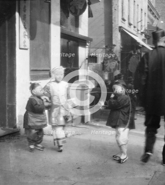 Three children standing on a sidewalk, Chinatown, San Francisco, between 1896 and 1906. Creator: Arnold Genthe.