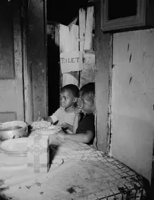 Three children waiting in the kitchen while their mother prepares the..., Washington, D.C, 1942. Creator: Gordon Parks