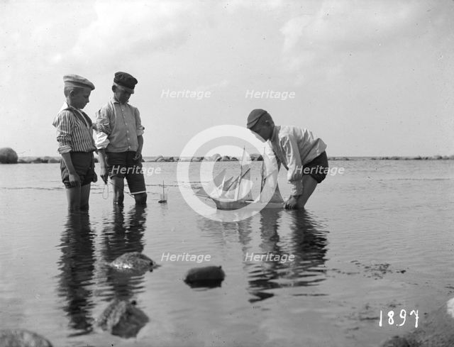 Three boys playing with a model sailing ship, 1897. Creator: Unknown.