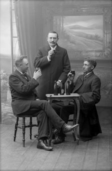 Three men having a beer, posed in a photographer's studio, Landskrona, Sweden, 1910. Creator: Unknown