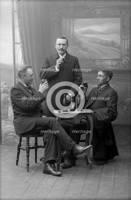 Three men having a beer, posed in a photographer's studio, Landskrona, Sweden, 1910. Creator: Unknown.