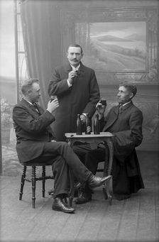 Three men having a beer, posed in a photographer's studio, Landskrona, Sweden, 1910