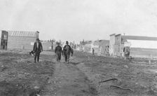 Three men walking down a dirt road, through town, between c1900 and 1916. Creator: Unknown