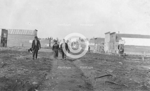 Three men walking down a dirt road, through town, between c1900 and 1916. Creator: Unknown.