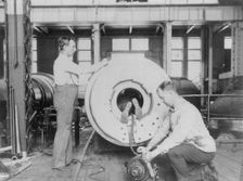 Three men working on large gun in Naval Gun Factory, Washington, D.C., one of the men lying..., 1903 Creator: Frances Benjamin Johnston