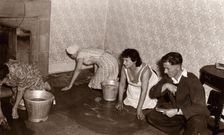 Three women scrub a stone floor on their hands and knees, 1956