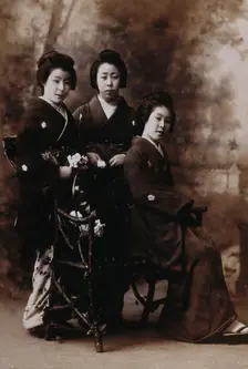 Three young women posing in a photographic studio, one seated on a bench..., early 20th century. Creator: Unknown