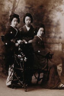 Three young women posing in a photographic studio, one seated on a bench..., early 20th century. Creator: Unknown