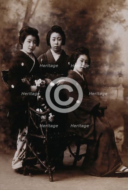 Three young women posing in a photographic studio, one seated on a bench..., early 20th century. Creator: Unknown.