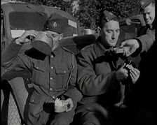 Two Male British Soldiers Sitting at the Front of Army Trucks and Eating While Two Others..., 1939. Creator: British Pathe Ltd