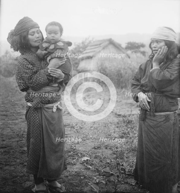 Two Ainu woman, one holding a child, standing outside, 1908. Creator: Arnold Genthe.