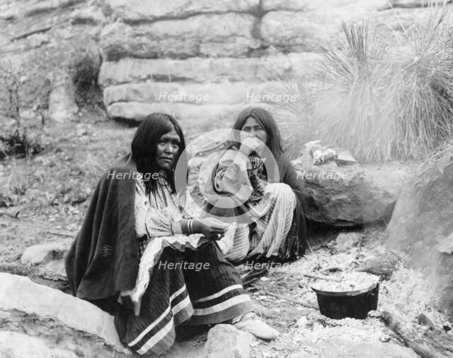 Two Apache Indian women at campfire, cooking pot in front of one, c1903. Creator: Edward Sheriff Curtis.