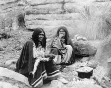 Two Apache Indian women at campfire, cooking pot in front of one, c1903. Creator: Edward Sheriff Curtis