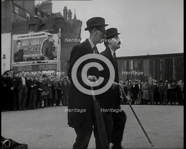 Two British Men in Suits and Hats Dancing in a Square With Men and Woman Watching Them..., 1938. Creator: British Pathe Ltd.