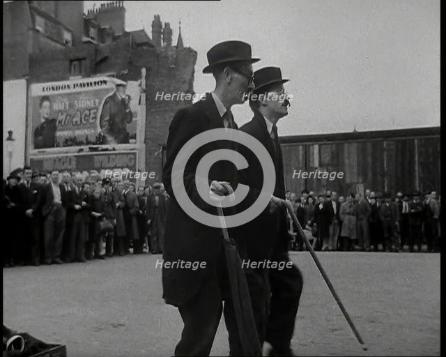 Two British Men in Suits and Hats Dancing in a Square With Men and Woman Watching Them..., 1938. Creator: British Pathe Ltd.