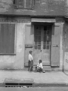 Two children outside a door with shutters in the French Quarter, New Orleans, between 1920 and 1926. Creator: Arnold Genthe