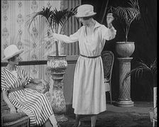 Two Female Civilians Leisuring in a Drawing Room Wearing Long Dresses and Hats Comparing..., 1920. Creator: British Pathe Ltd