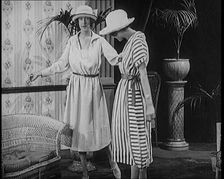 Two Female Civilians Leisuring in a Drawing Room Wearing Long Dresses and Hats Comparing..., 1920. Creator: British Pathe Ltd