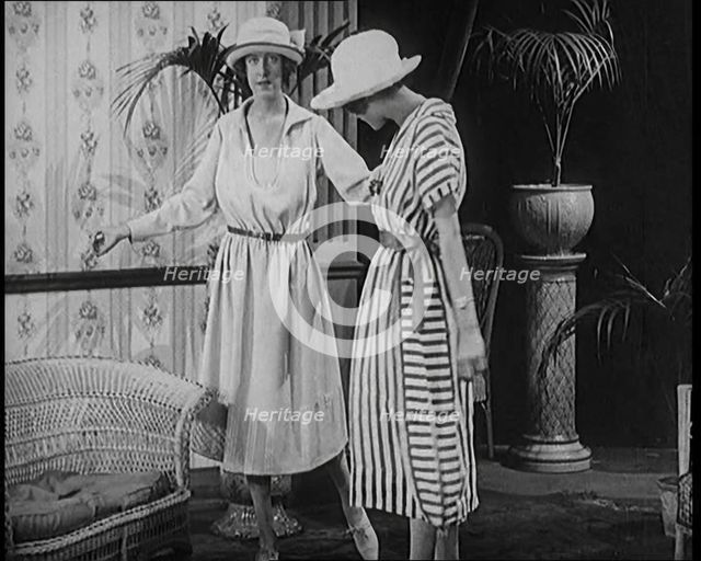 Two Female Civilians Leisuring in a Drawing Room Wearing Long Dresses and Hats Comparing..., 1920. Creator: British Pathe Ltd.
