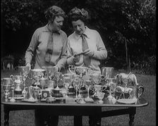Two Female Civilians Standing Behind a Table Loaded with Trophies, 1920. Creator: British Pathe Ltd
