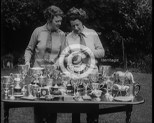 Two Female Civilians Standing Behind a Table Loaded with Trophies, 1920. Creator: British Pathe Ltd.