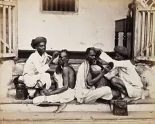 Two Indian barbers wearing turbans shaving the heads of two Indian men..., c1900s. Creator: Unknown