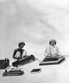 Two Indian bookbinders: one trimming page edges in a press, the other decorating a binding. Creator: Unknown