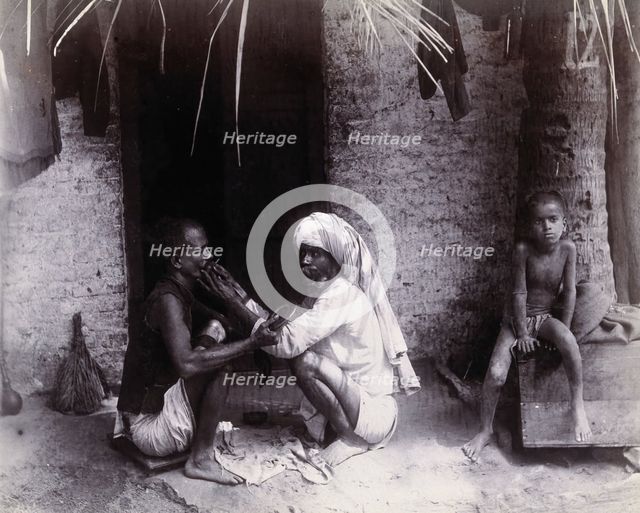 Two Indian men crouching; one is cutting the other's hair, while a girl sits.., c1890s.  Creator: Unknown.