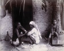 Two Indian men crouching; one is cutting the other's hair, while a girl sits.., c1890s. Creator: Unknown