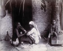 Two Indian men crouching; one is cutting the other's hair, while a girl sits.., c1890s. Creator: Unknown