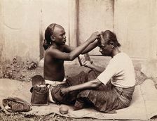 Two Indian men sitting cross-legged; one appears to be a barber..., c1890s. Creator: Unknown
