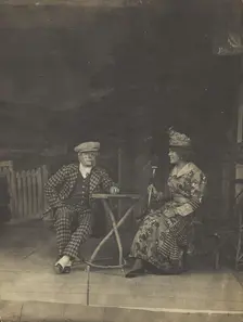 Two sailors, one in drag, sit on stage at a table, in front of very detailed scenery (1910-1919?). Creator: Unknown