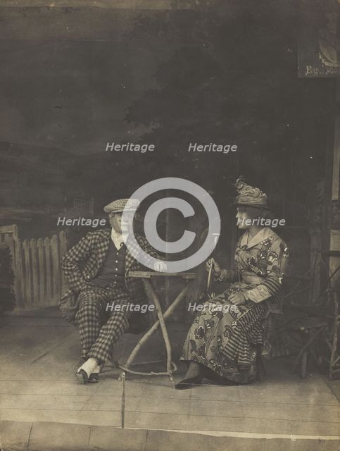 Two sailors, one in drag, sit on stage at a table, in front of very detailed scenery (1910-1919?). Creator: Unknown.