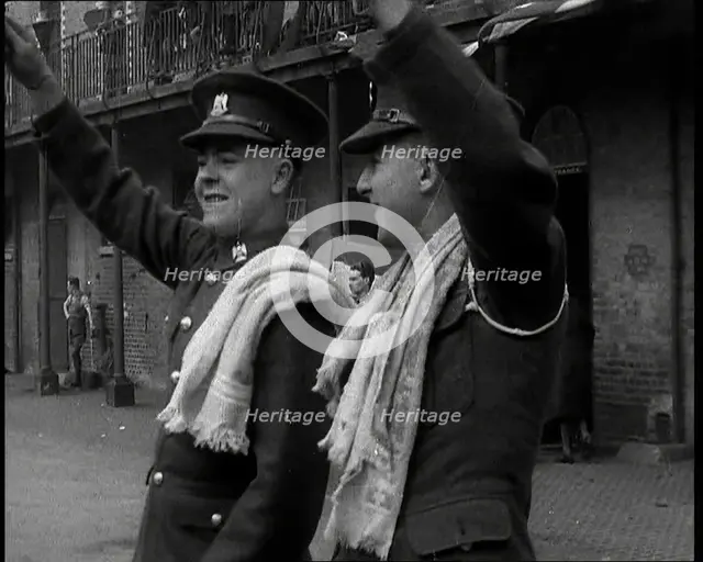 Two Uniformed British Soldiers With Arms Raised Standing Outside Brick Building, 1937. Creator: British Pathe Ltd.