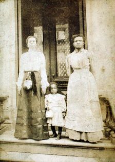 Two women and a child standing on step in front of a doorway of a house, c1900. Creator: Eckehard Munck