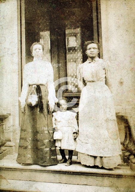 Two women and a child standing on step in front of a doorway of a house, c1900. Creator: Eckehard Munck.
