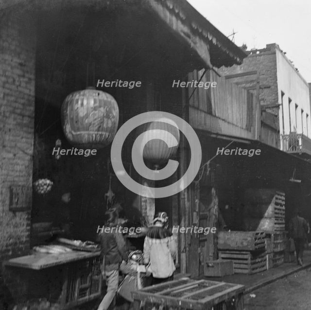 Two women and a child walking down a sidewalk betwen crates, Chinatown, San Francisco, c1896-1906. Creator: Arnold Genthe.