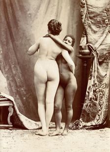 Two women posing naked in a photographic studio, standing embracing each other in front..., c1900. Creator: Unknown
